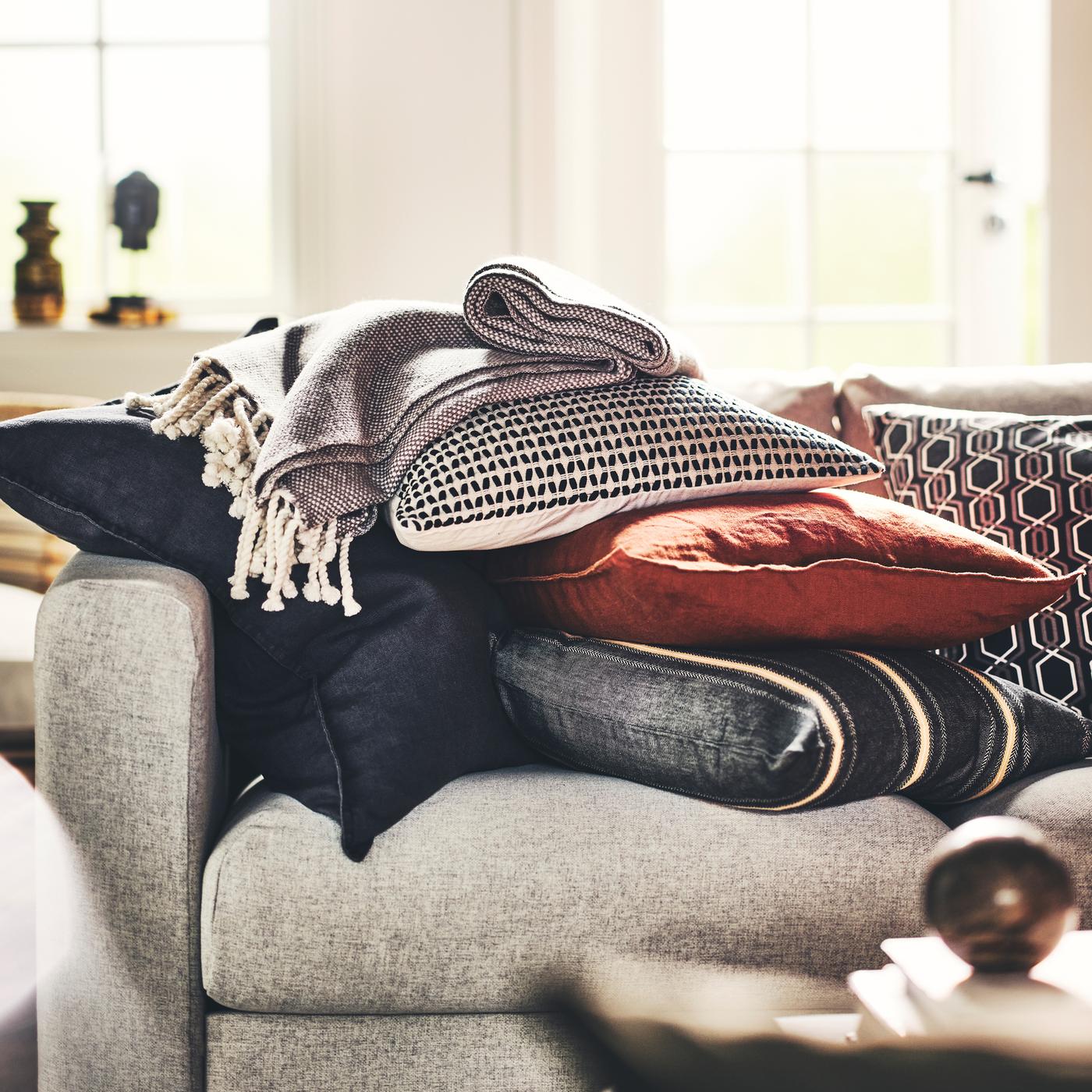 Un plaid et une pile de coussins habillés de housses KUSTFLY et DYTÅG, sur un canapé beige.