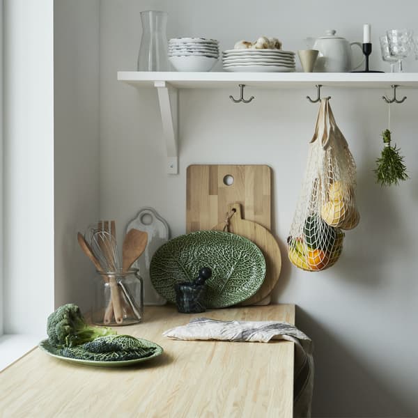Un plan de travail de cuisine en bois avec une assiette en forme de feuille, des planches à découper en bois et de la vaisselle sur une étagère.