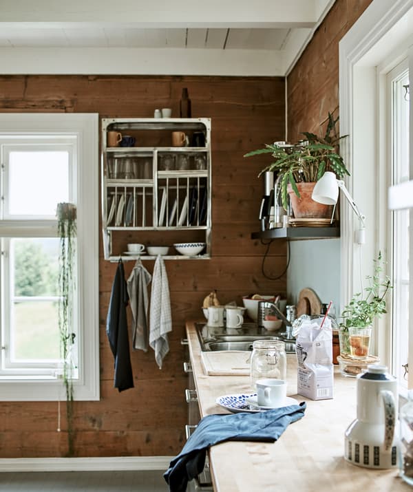 Un plan de travail en bois dans une cuisine lambrissée avec des rangements ouverts comprenant une armoire murale de style industriel remplie de vaisselle.