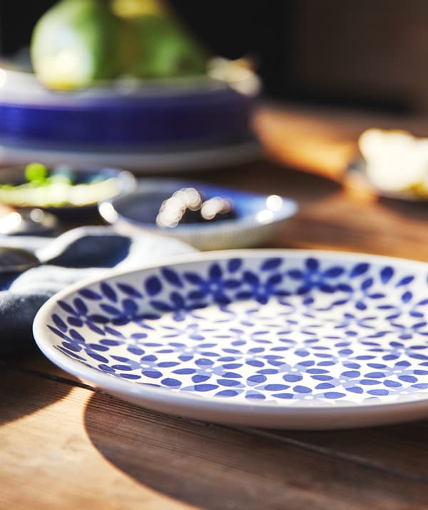 Un plato floral azul y blanco sobre una mesa de madera junto a una pila de platos.