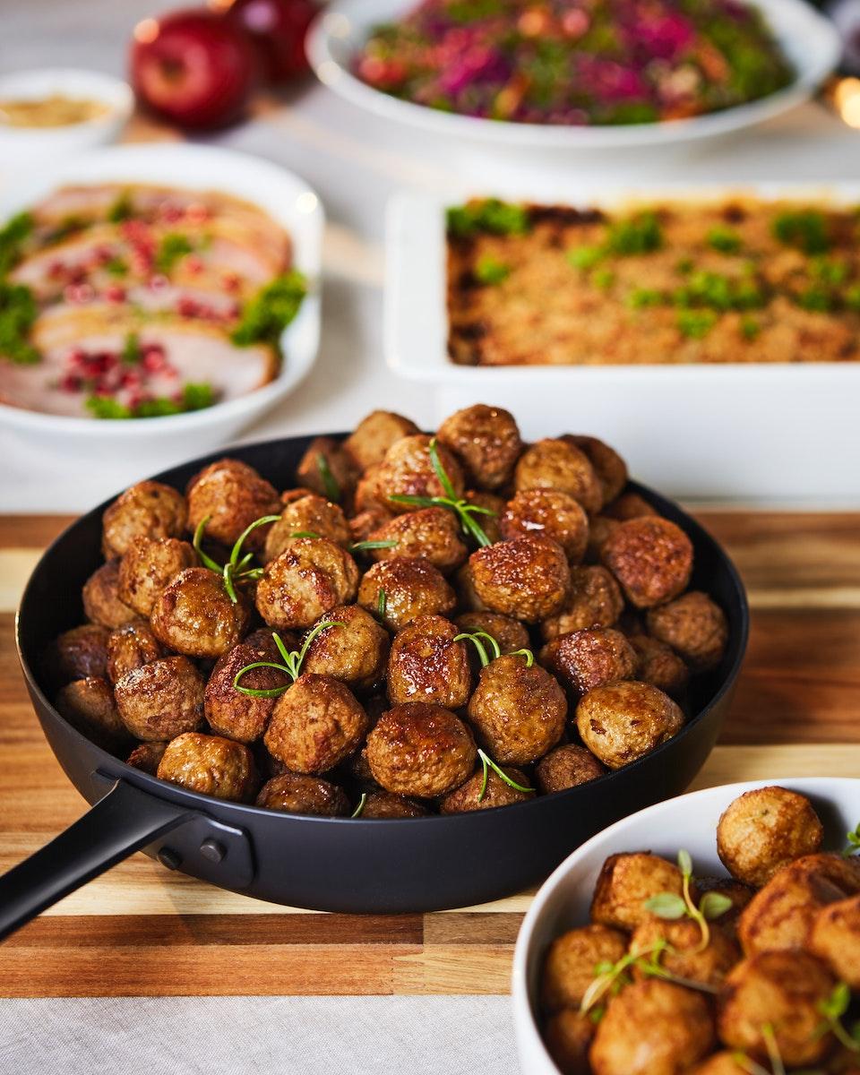 Un plato negro con albondigas vegetales, todo sobre una tabla para cortar, hierbas y otras preparaciones a su lado.