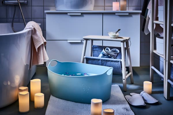 Un portabiancheria TORKIS con all'interno dell'acqua pronto per un pediluvio. accanto, alcune candele con luci a led.