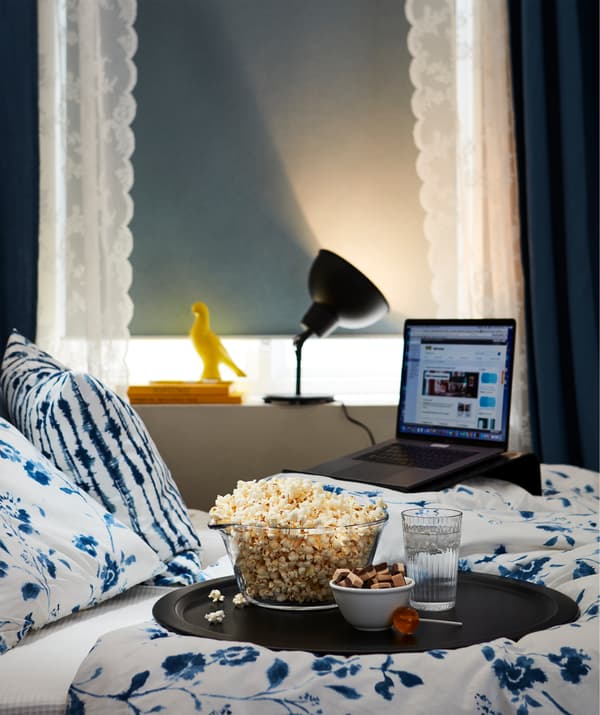 Un portatile su un apposito supporto, tende abbassate, una lampada accesa lontano dal letto e un vassoio con degli snack trasformano la camera da letto in un cinema.