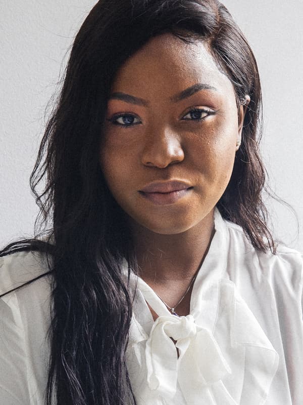 Un primo piano di Precious, una rifugiata proveniente dalla Nigeria che ora lavora presso IKEA Canada e che sorride all’obiettivo con indosso una camicia bianca – IKEA
