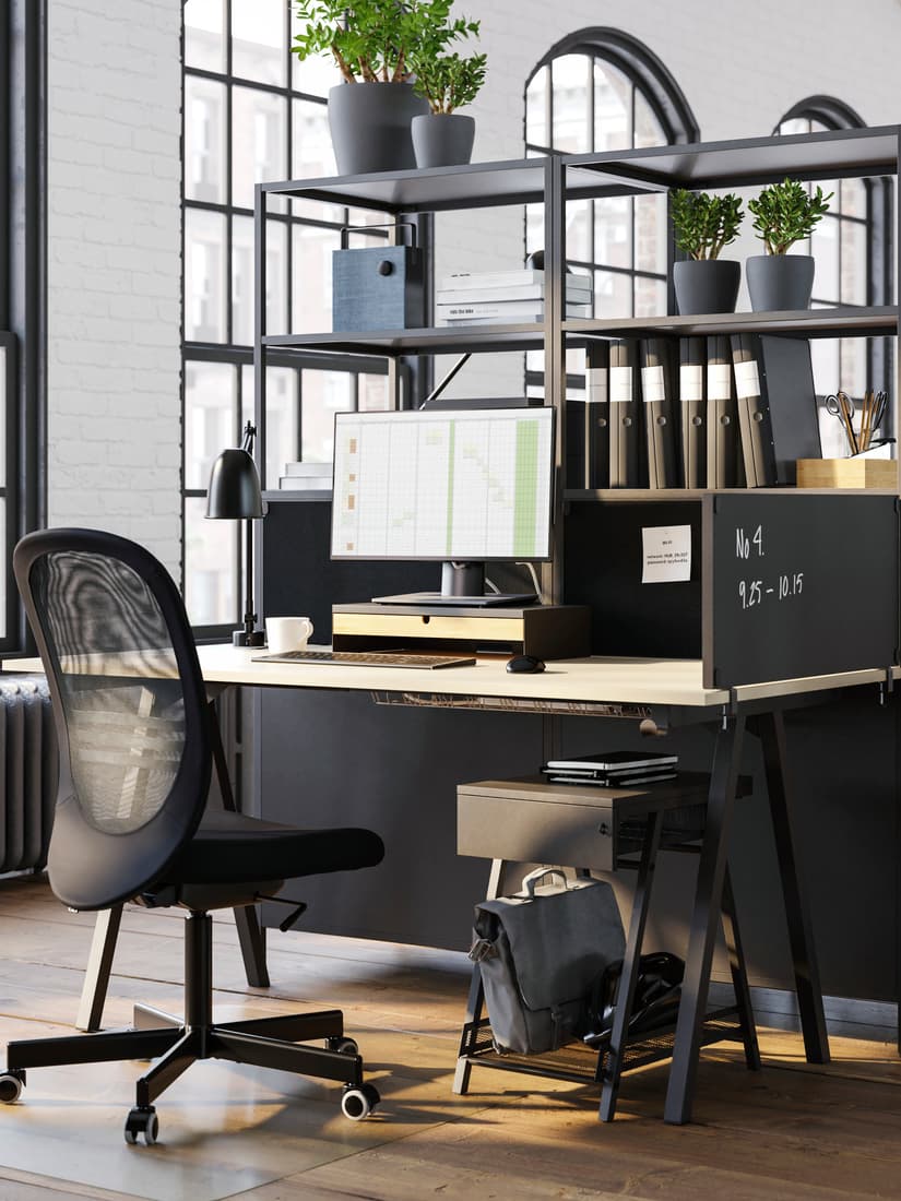 Un puesto de trabajo con silla TROTTEN, amoblado con un escritorio y una repisa con documentos y decoración. Sobre el escritorio se ve una pantalla y un teclado.