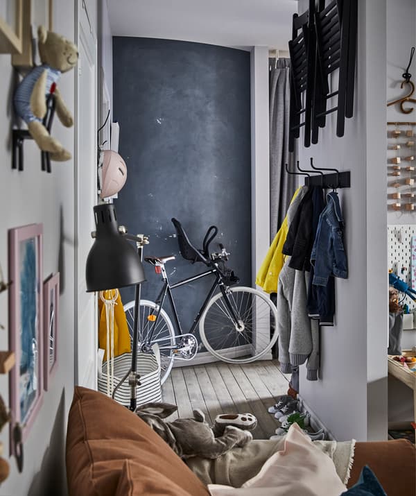 Un rebedor amb roba i cadires plegables que estan penjades a la paret, una bicicleta i una paret de pissarra.
