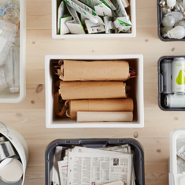 Un recipiente de plástico KLÄMTARE rodeado doutras caixas de almacenamento, cheas de produtos reciclables, sobre unha superficie de madeira.