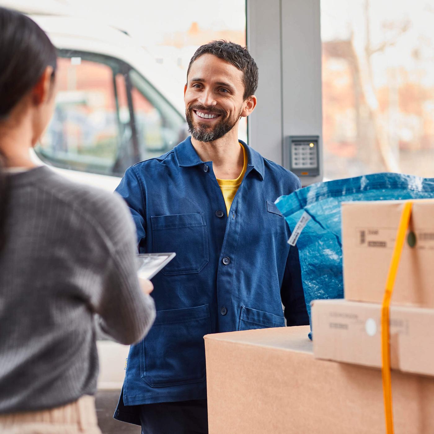 Un repartidor sonriéndole a una clienta y entregándole cajas IKEA.