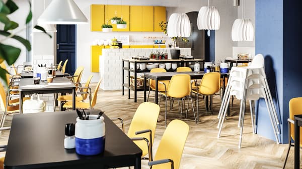 Un restaurant lumineux avec des chaises jaune foncé, des tables noires, des chaises d’enfants blanches, des armoires jaunes et des suspensions blanches.