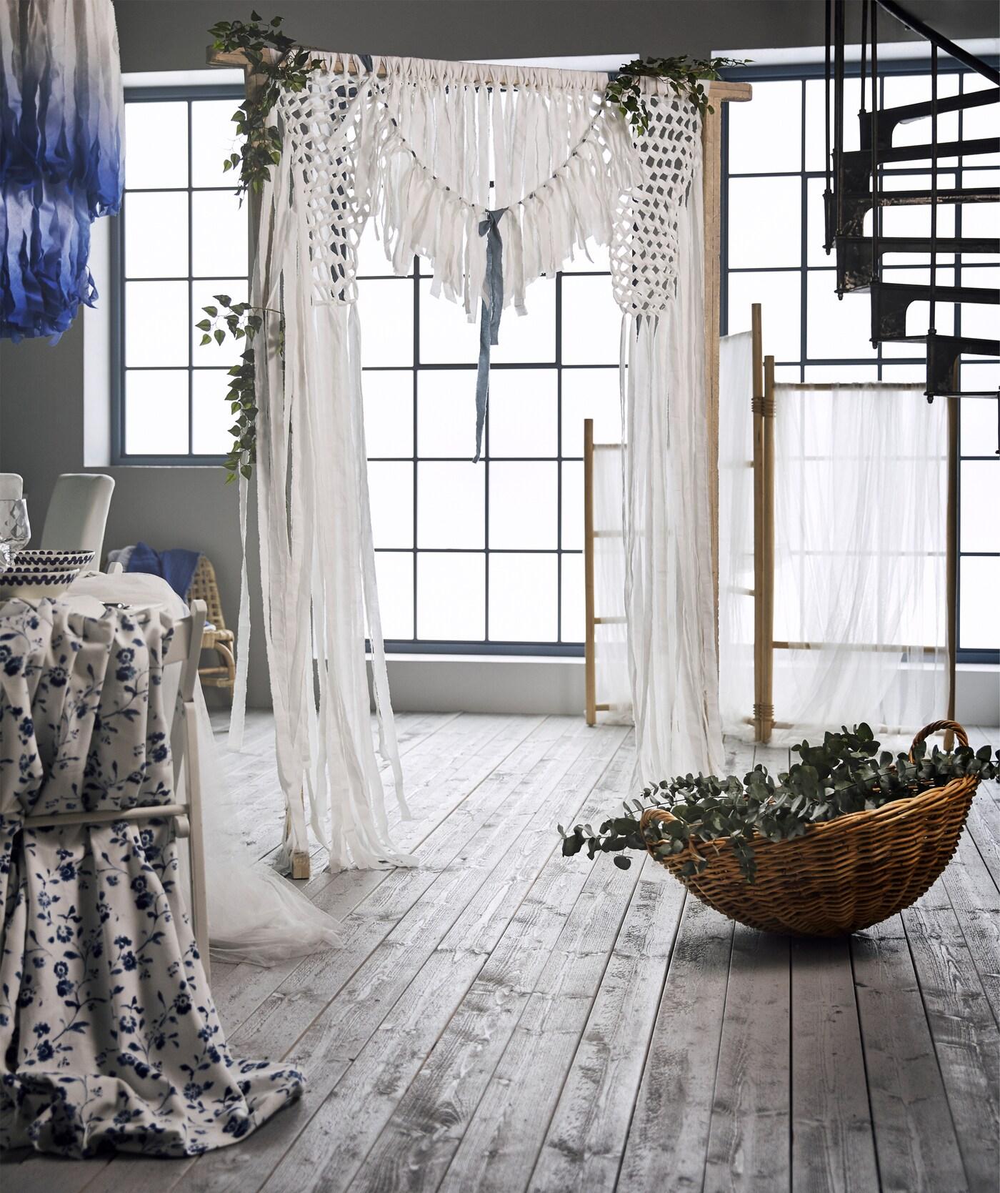 Un rideau de mariage réalisé à partir de bandes de tissu en coton blanc attachées à un paravent en rotin TÄNKVÄRD.