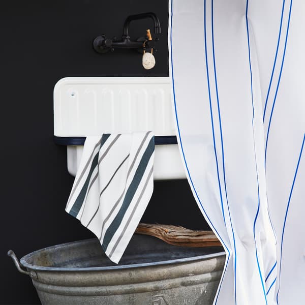 Un robinet noir au-dessus d'un lavabo blanc, avec serviette et rideau de douche à rayures et un seau en métal en dessous