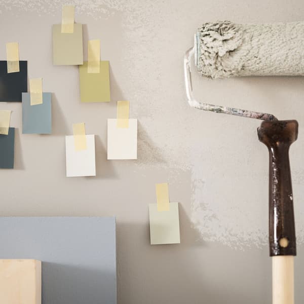 Un rullo per dipingera la parete di bianco con accanto dei bigliettini di diversi colore.