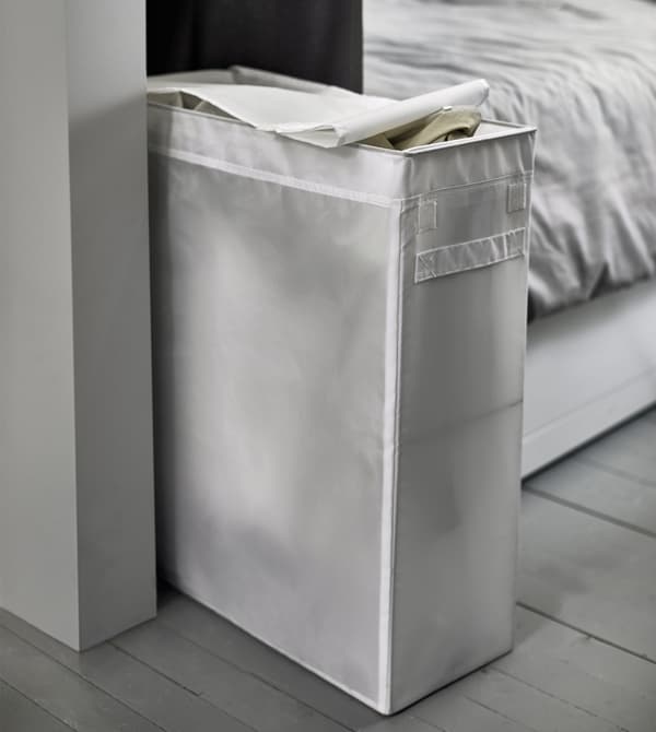 Un sac à linge blanc étroit est installé au pied du lit.