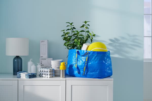 Un sac bleu IKEA rempli est posé sur un buffet, près d’autres produits IKEA venant d’être achetés.