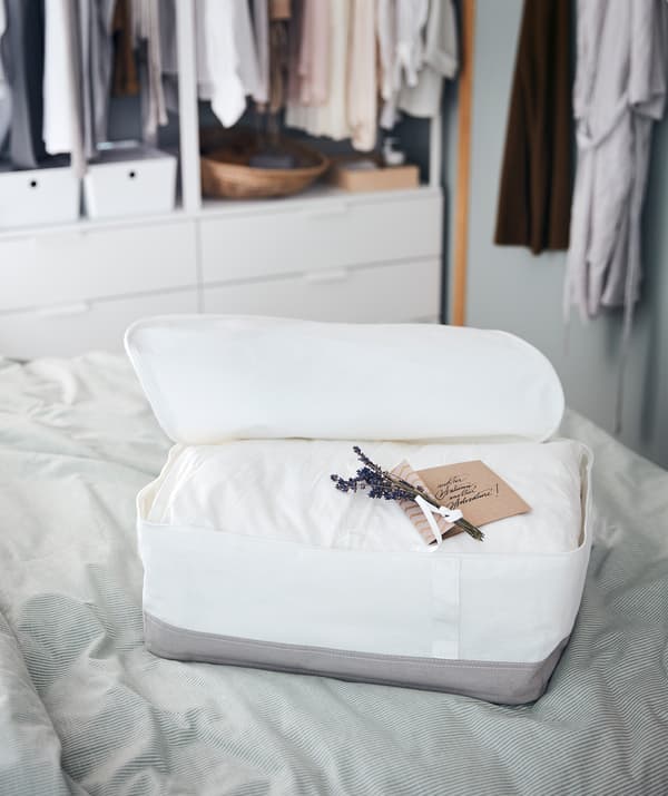 Un sac de rangement posé sur un lit contenant une couette épaisse avec dessus une jolie note manuscrite et quelques brins de lavande.