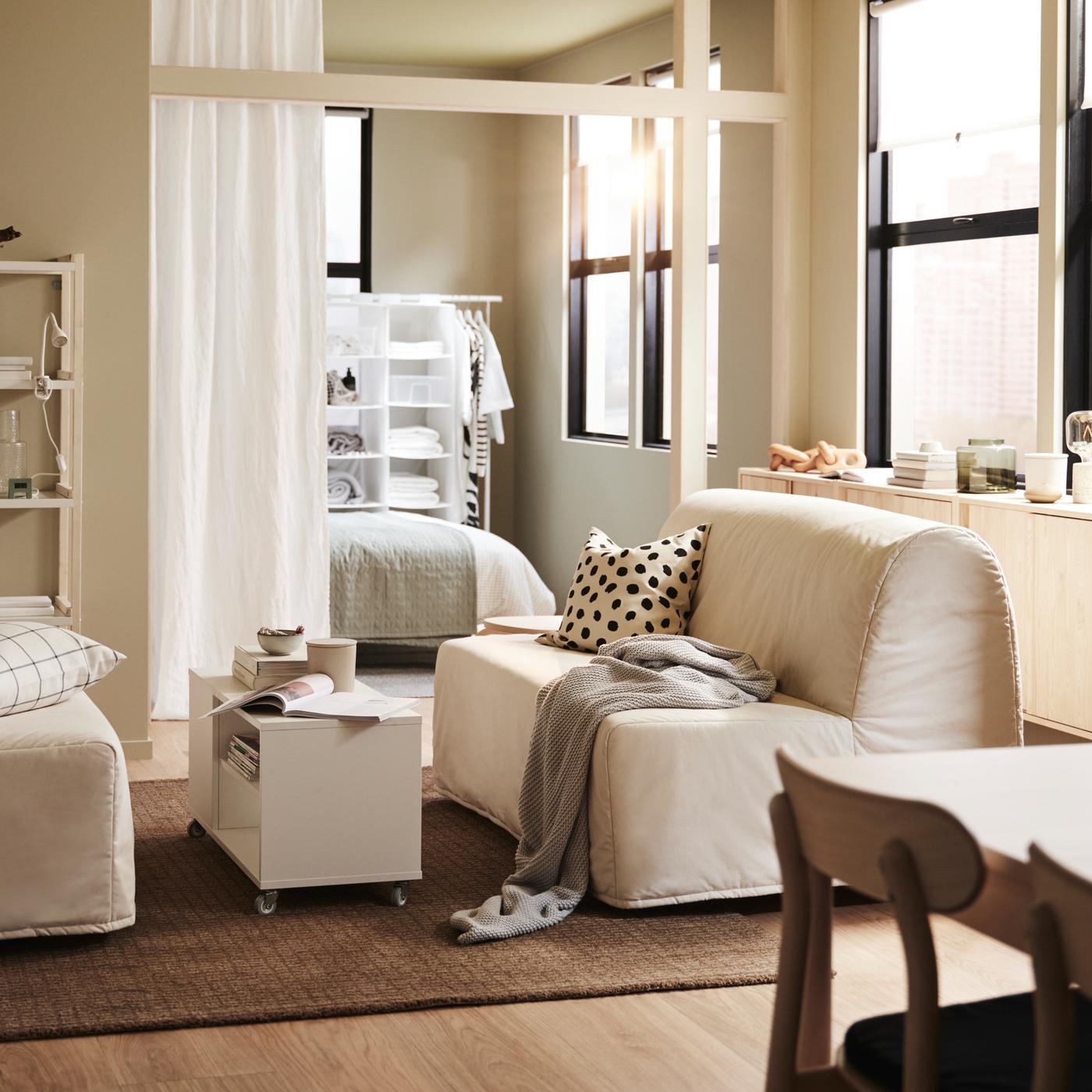 Un salon avec deux canapés convertibles LYCKSELE LÖVÅS sur un tapis en jute, une table basse VIHALS blanche et une étagère en blanc/peuplier.