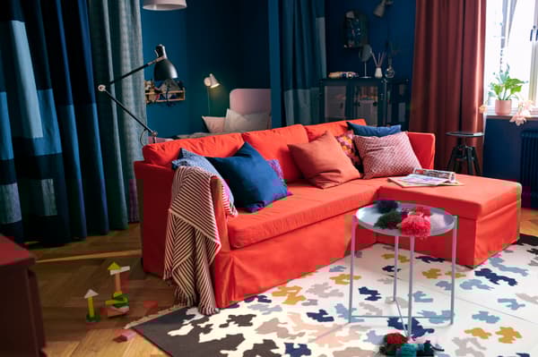 Un salón con un sofá rojo y una alfombra de lana de IKEA hecha a mano con muchos colores y muy alegre. Un salón de estilo moderno.