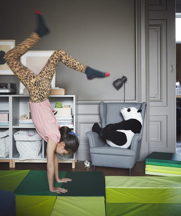 Un salon gris avec des tapis de jeu vert vif et une fille qui fait le poirier.