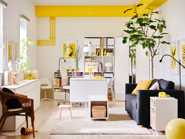 Un salon lumineux avec des touches de jaune vif, dans lequel il y a des rangements VIHALS blancs et un canapé-lit PÄRUP gris foncé.