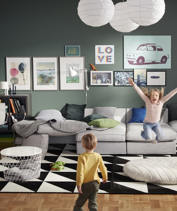 Un salon vert avec un grand canapé modulaire gris et deux enfants qui jouent.