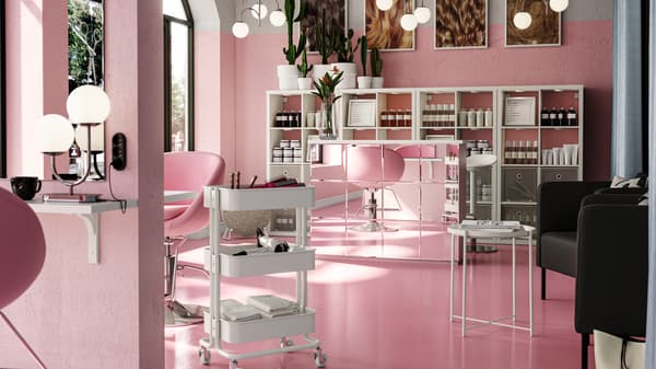 Un salone da parrucchiere arioso con pareti e dettagli rosa e con scaffali KALLAX bianchi dietro una reception con mobili a specchio. Un carrello RÅSKOG si trova accanto a una postazione di lavoro.