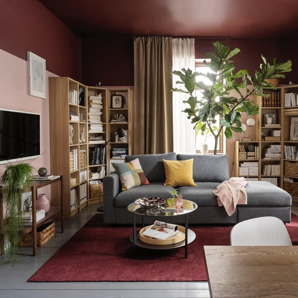 Un salotto con un divano angolare al centro e due librerie appoggiate alla parete. Davanti un tavolino nero e uno scaffale. Gli arredamento sono stile pastello.