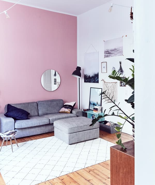 Un séjour au plafond haut, un mur rose et un canapé gris avec un repose-pieds.