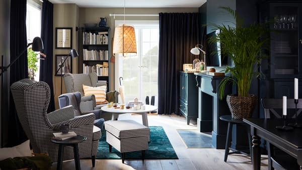 Un séjour avec deux fauteuils à oreilles à motif pied-de-poule, tapis vert, suspension en bambou et table basse ronde.