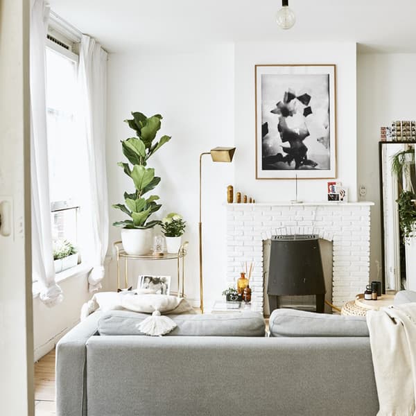 Un séjour blanc avec un canapé, une cheminée et des plantes.