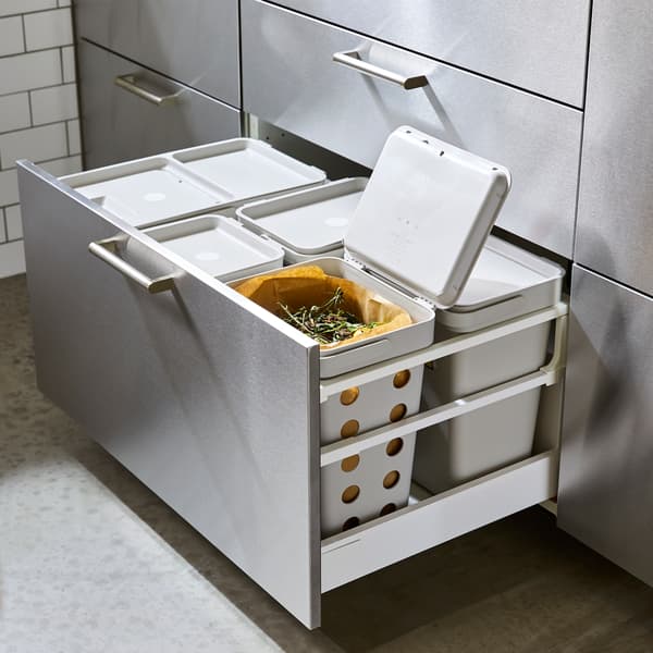 Un sertar de bucătărie deschis cu un front din oțel inoxidabil. Coșurile de sortare a deșeurilor gri se află în interior, iar unul este prevăzut cu găuri de aerisire.