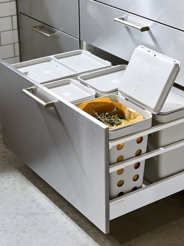 Un sertar de bucătărie mare tras în care se află o soluție completă de sortare a deșeurilor HÅLLBAR, unul cu capacul deschis sub care se văd resturi alimentare.