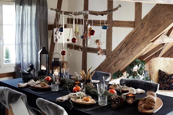 Un service de table de Noël rustique et chaleureux avec une nappe noire, des assiettes noires, des planches de bois et des branches de la forêt.