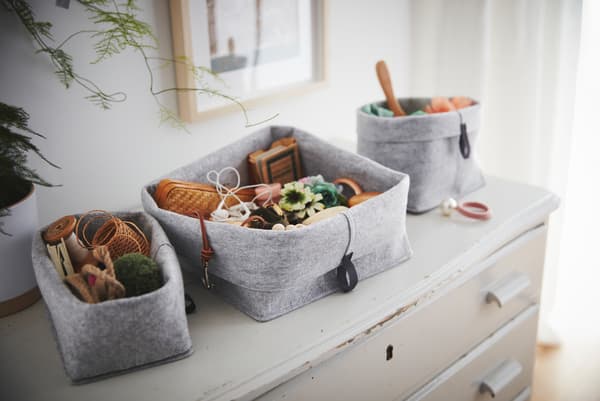 Un set de corbeilles en tissu remplies de bibelots et objets divers posé sur une vieille commode usée.