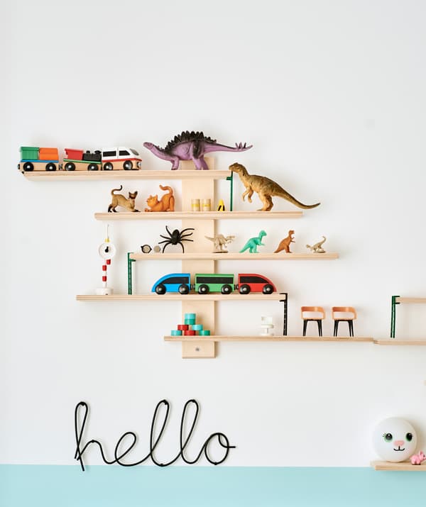 Un set de rafturi din lemn cu jucării, inclusiv dinozauri și trenuri. Dedesubt, un semn din metal negru cu textul „hello”.