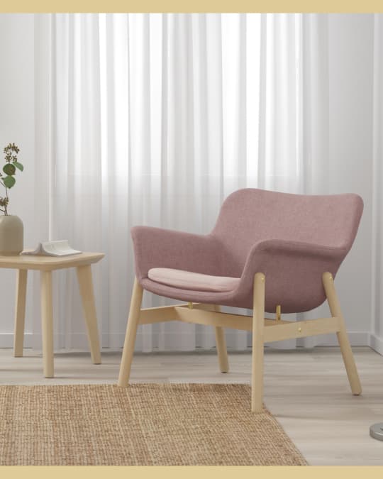 Un sillón IKEA rosa tapizado con patas de madera al costado de una sala con un gran tapete.