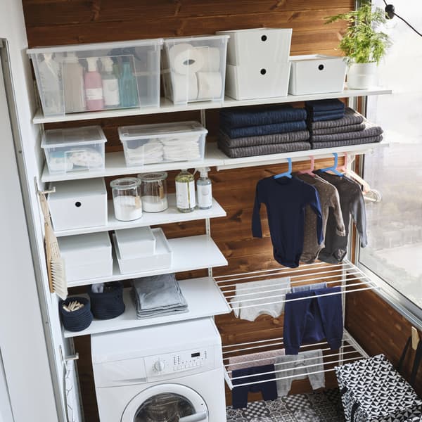 Un sistema componibile bianco con ripiani, due stendibiancheria e un bastone appendiabiti con dei vestiti da bambino appesi ad asciugare - IKEA