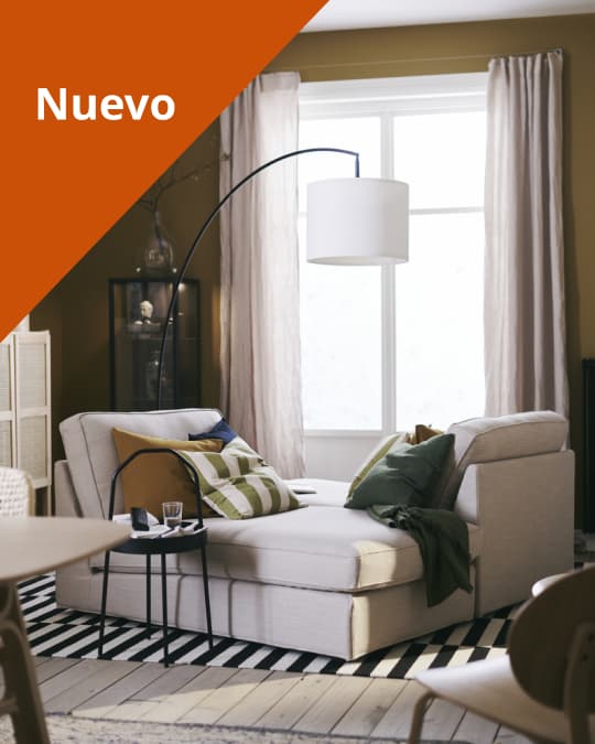 Un sofá beige sobre una alfombra IKEA y por el costado una lámpara de pie.