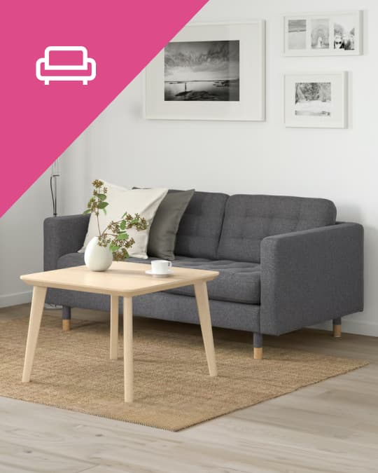 Un sofá de 3 cuerpos gris con dos cojines sobre un tapete IKEA.