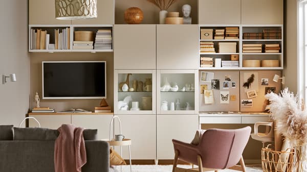 Un soggiorno arredato con un sistema componibile BESTÅ grigio-beige con elementi a giorno e con ante, un divano, una TV e una postazione di lavoro - IKEA
