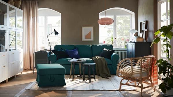 Un soggiorno con divano e poggiapiedi turchese scuro, una combinazione di mobili bianchi e un mobile blu-verde scuro.