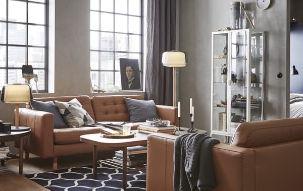 Un soggiorno con due divani in pelle marrone, un tavolino, una vetrina e alcune lampade - IKEA