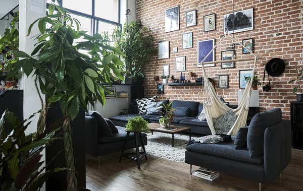Un soggiorno con i soffitti alti, una parete con mattoni a vista e un divano componibile grigio – IKEA