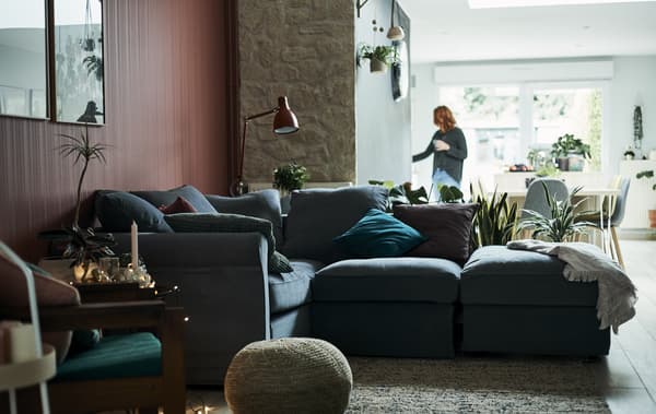 Un soggiorno con un divano a L grigio e una parete rossa e la zona pranzo sullo sfondo – IKEA
