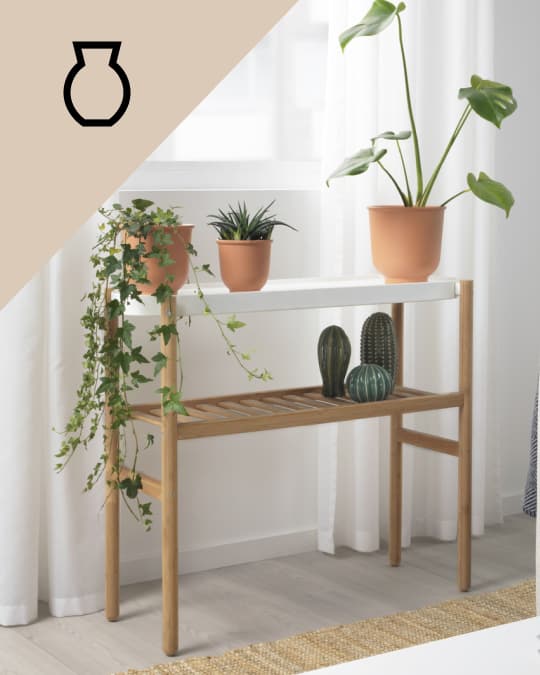 Un soporte para planta de dos niveles con decoraciones en la bandeja inferior y materas con plantas en la bandeja superior.