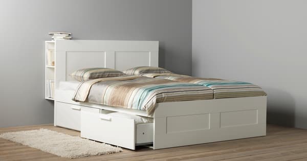 Un struttura letto con contenitori e testiera, bianca BRIMNES serie. Il letto ha lenzuola e federe colorate.