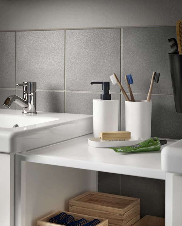 Un suport pentru periuțe de dinți cu trei periuțe, un dozator de săpun și o tăviță în combinația alb/negru pe un corp lipit de un suport de lavoar.