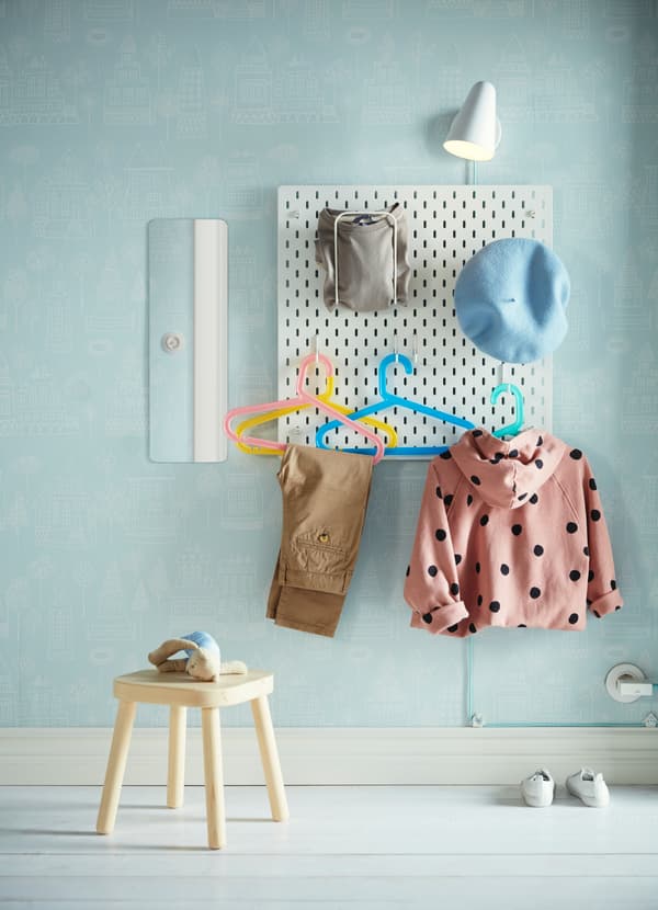 Un tablero perforado de IKEA SKADIS donde hay colgada ropa de niño y una mochila.