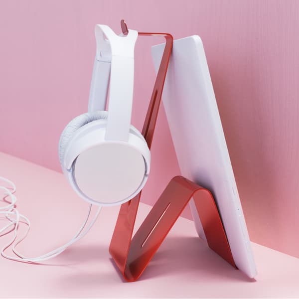 Un tablet e un paio di cuffie bianche su un supporto rosso davanti a una parete rosa - IKEA