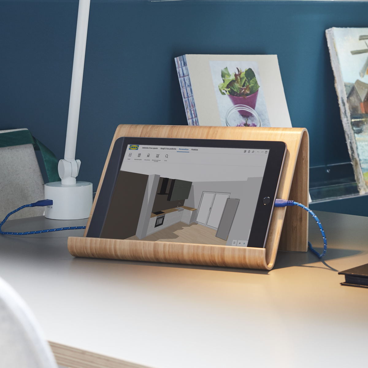 Un tablet su un supporto impiallacciato in bambù su un piano di lavoro bianco. Sul tablet è visibile il configuratore cucine IKEA in funzione.