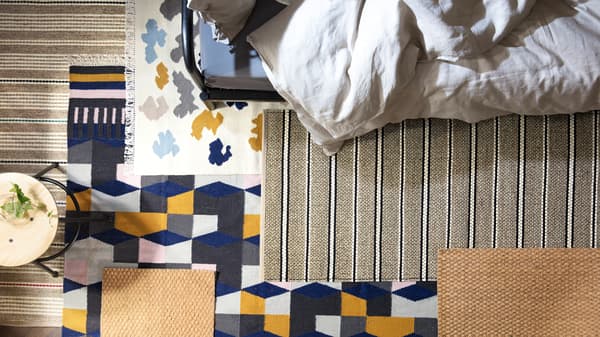 Un tabouret et le bord d’un lit FYRESDAL sur un plancher avec beaucoup de tapis aux différents motifs qui se chevauchent.